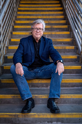 Logan Enright sitting on an exterior staircase jeans and a sport coat.